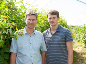 Tim Place (left), third generation of the Place family, and his son Ben Place (right, standing side by side among raspberry canes inside a polytunnel at Church Farm, Tunstead, Norfolk, in the 2010s.